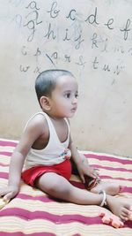 Cute boy looking away while sitting on bed