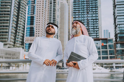 Men wearing dish dash standing against buildings in city