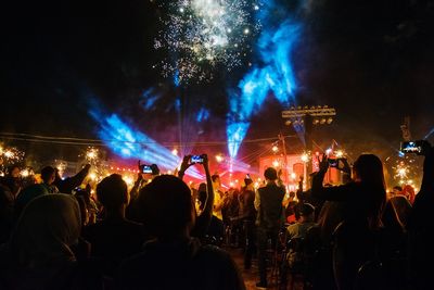 Rear view of people enjoying concert against firework display at night