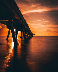 Silhouette pier over sea against orange sky