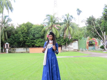 Portrait of woman standing on field against trees