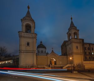 Light trails on building against sky at dusk