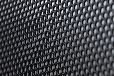 Macro shot of a black metal surface with round holes, gray background.