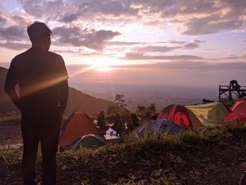 Rear view of man sitting on tent against sky during sunset