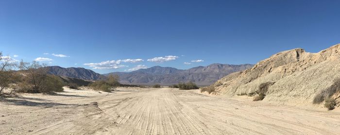 Panoramic view of dirt road by mountains against blue sky