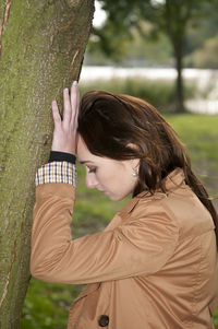 Side view of woman standing by tree trunk in park