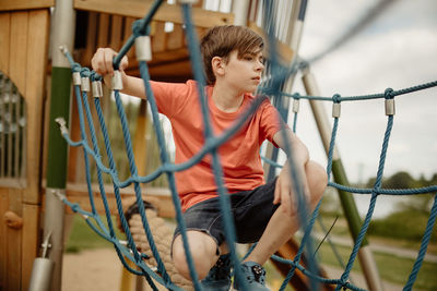 Teen boy rest at playground rope watch out for other kids and have thoughts while having a mean idea