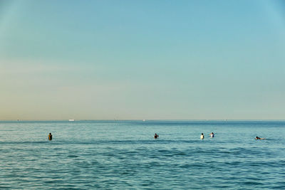 People swimming in sea against clear sky