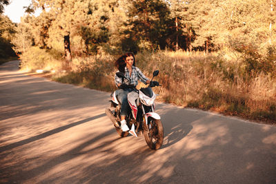 Young confident woman riding motorcycle on country road in forest