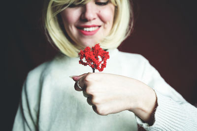 Close-up of woman holding red flower against brown background
