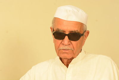 Portrait of senior man wearing sunglasses and cap against wall