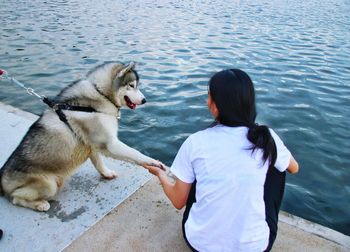 Rear view of woman holding dog paw at lakeshore