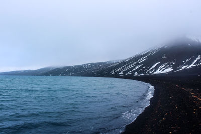 Scenic view of sea by snowcapped mountains against sky