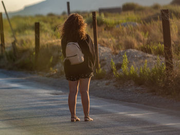 Rear view of woman with backpack standing on road at sunset