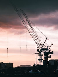 Silhouette cranes at construction site against sky during sunset