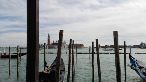 Wooden posts in sea against cloudy sky