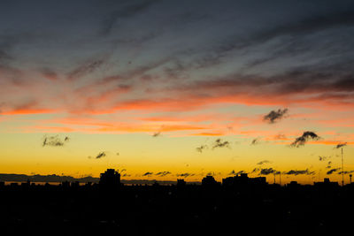 Silhouette buildings against dramatic sky during sunset