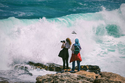 People standing on rock by sea