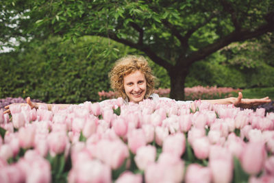Portrait of smiling woman with pink flowers against trees