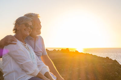People sitting on rock against sky during sunset