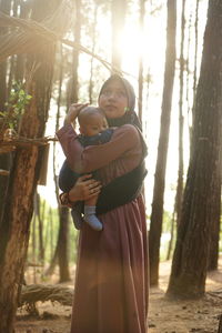 Young woman holding son while standing amidst trees on field