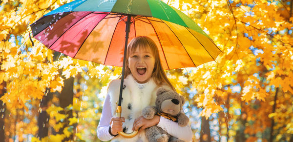 Portrait of cute girl holding umbrella against maple tree