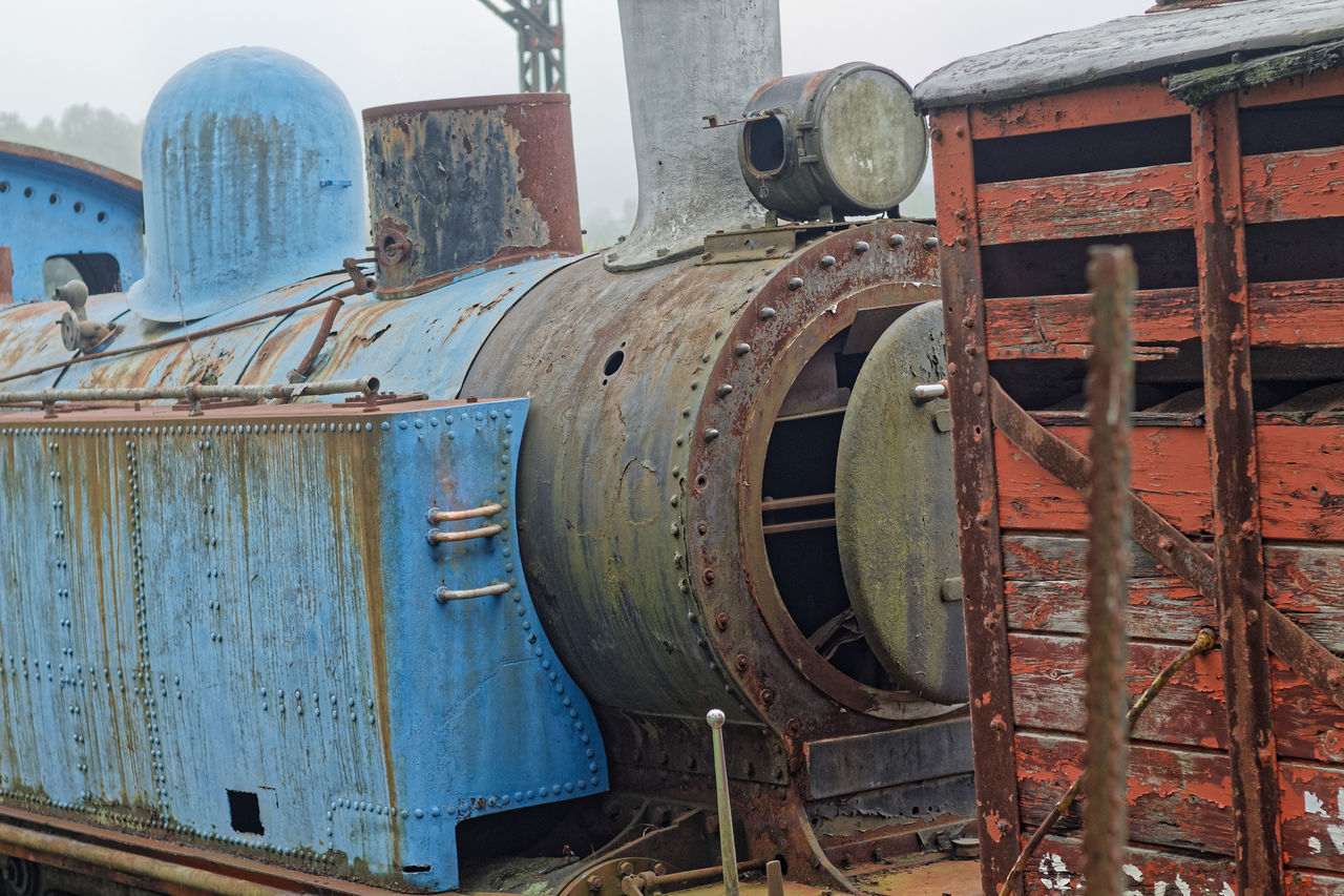 CLOSE-UP OF RUSTY TRAIN AGAINST OLD RAILROAD STATION