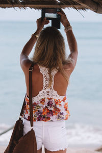 Rear view of woman photographing while standing at beach