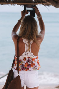 Rear view of woman photographing while standing on beach