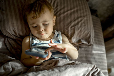 Cute toddler using smart phone lying in bed in bedroom