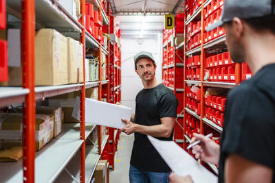 Warehouse worker holding box by colleague taking inventory at factory