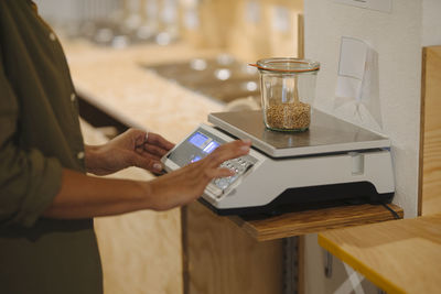 Midsection of female entrepreneur weighing grain jar on weight scale in cafe