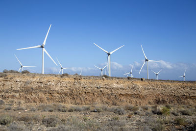 Windmills on field against clear blue sky