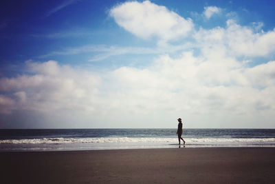 Teenage girl walking at beach against sky