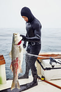 Full length of fisherman holding large fish while standing on boat in sea