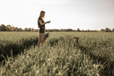 Young woman with dog standing on grassy field against clear sky