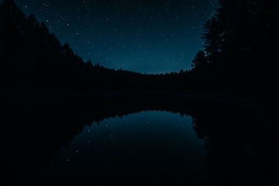 Reflection of silhouette trees in lake against sky at night