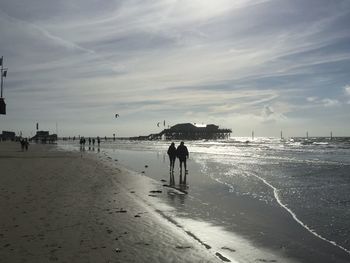 Silhouette people walking on beach against sky