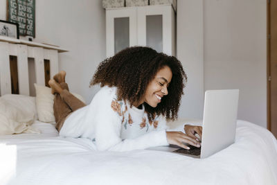 Young woman smiling while using laptop lying on bed at home