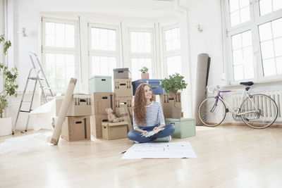 Woman surrounded by cardboard boxes sitting on floor with construction plan