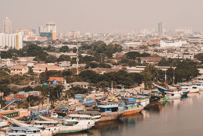 Boats moored in harbor by city against sky