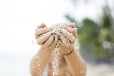 Close-up of shirtless man spilling sand against sky