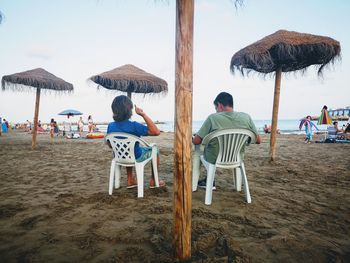 Rear view of people sitting on beach against sky