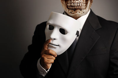 Midsection of man holding mask against gray background