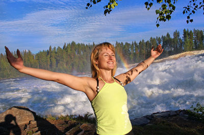 Happy young woman with arms raised against mountains