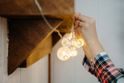 Cropped hands of woman hanging illuminated decorations on wall at home