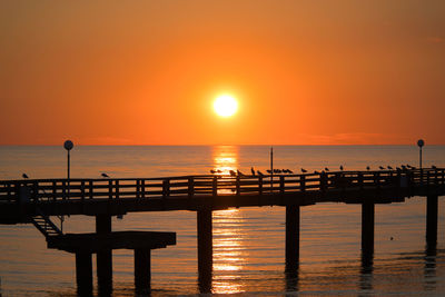 Silhouette pier over sea against sky during sunset