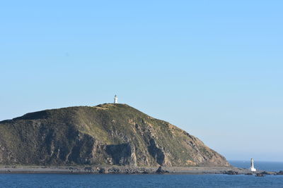 Lighthouse by sea against clear blue sky