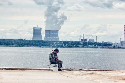 Men sitting at factory against sky