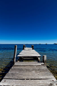 Pier over sea against clear blue sky